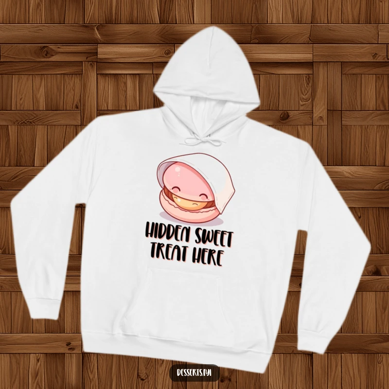 Funny hoodie featuring a curious macaron peeking from beneath a napkin, its filling subtly visible, a warm and humorous apparel choice.